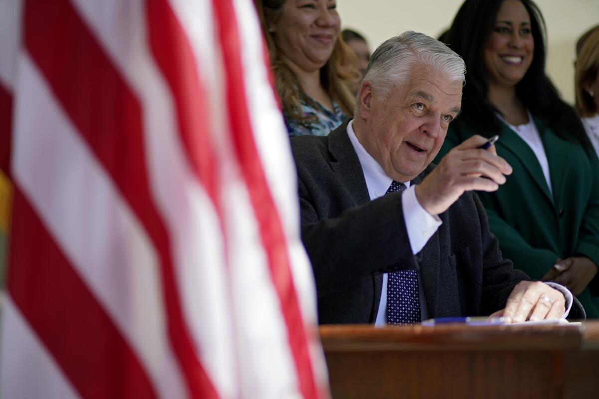 Gov. Steve Sisolak sits at a table holding a pen.