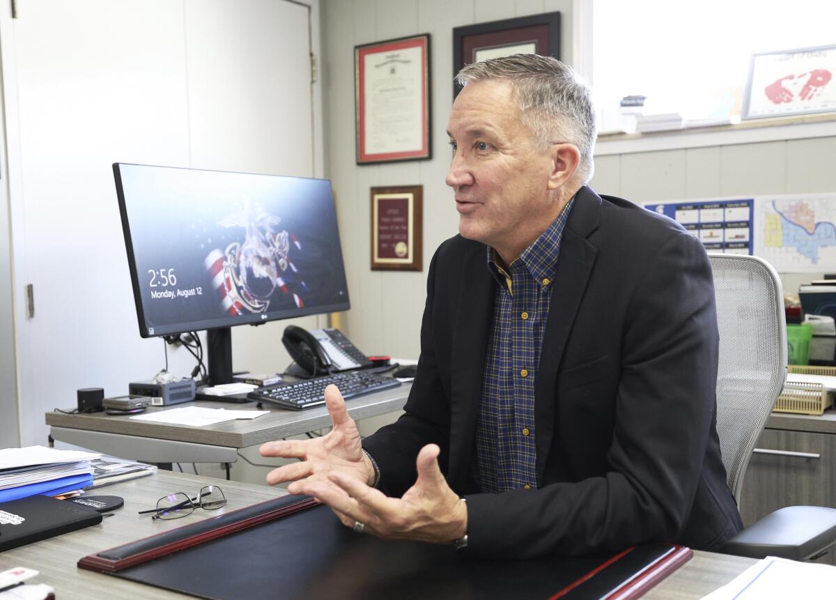 A man sits at a desk, gestures and speaks.