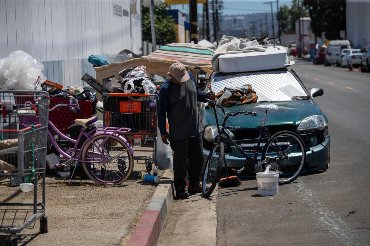 A man sweeping the street in front of a car and bicycles. 