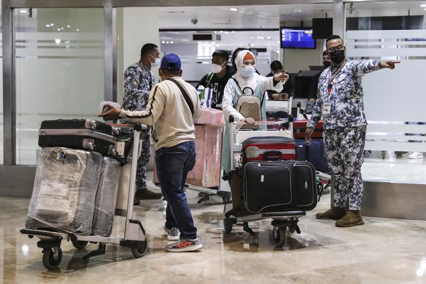 Members of the Philippine Coast Guard assist passengers as they arrive at Manila's International Airport, Philippines Thursday, Feb. 10, 2022. The Philippines lifted a nearly 2-year ban on foreign travelers Thursday in a lifesaving boost for its tourism and related industries as an omicron-fueled surge eases. (AP Photo/Basilio Sepe)