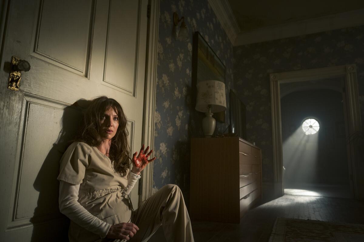 A woman sits with a raised bloody hand against a door in a scene from "Malignant."