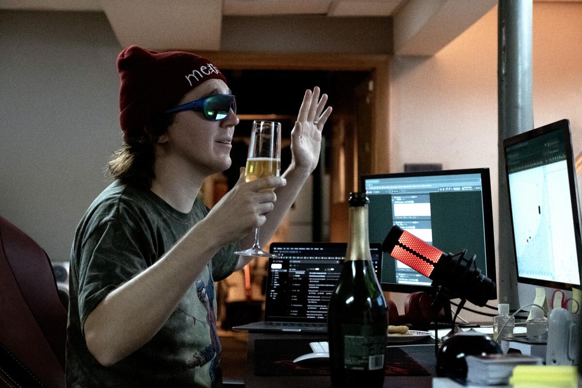 A man in a beanie and sunglasses holds a beer as live-streams his stock market advice show in "Dumb Money."