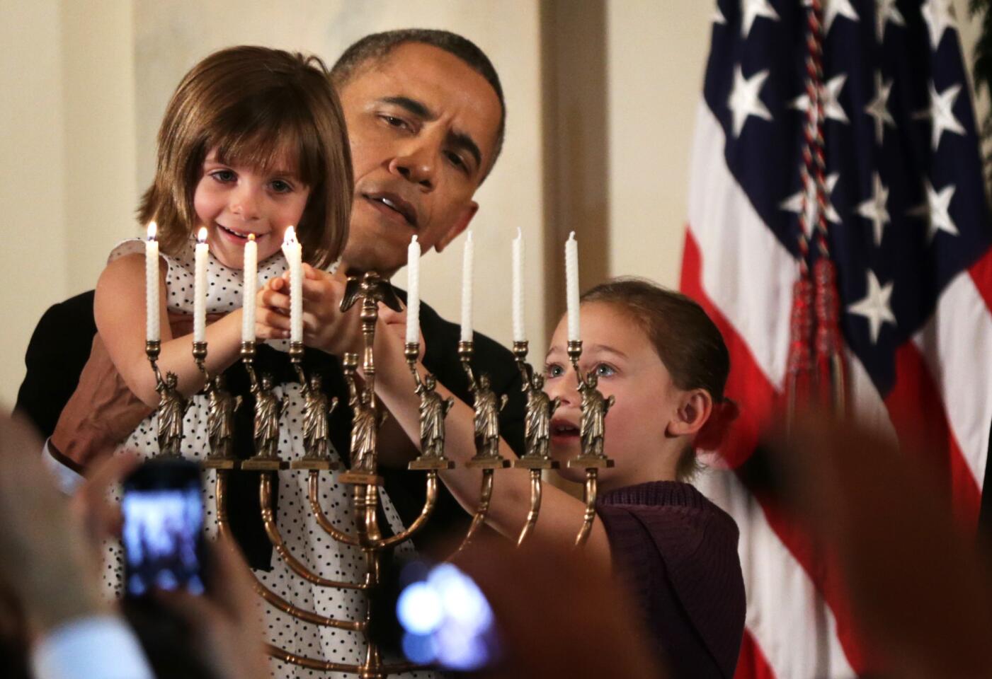 President Barack Obama holds up 4-year-old Kylie Schmitter, left, to light a menorah as Kylie's sister Lainey looks on during a Hanukkah reception at the White House in December 2013.