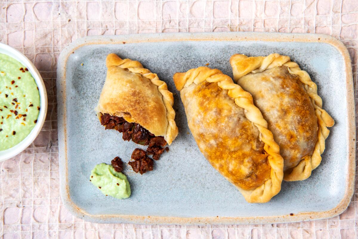 Two whole and one half vegan picadillo empanadas on a stoneware tray