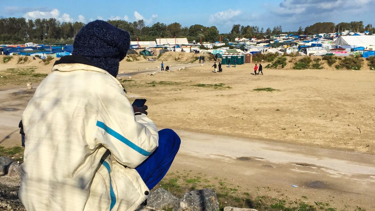 A young migrant glances at his cellphone while overlooking the "the Jungle."