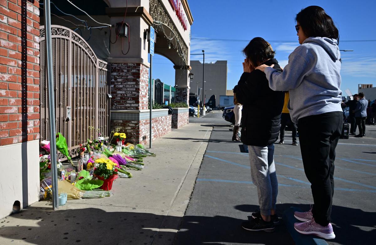Two women stand outside the Monterey Park shooting scene, where mourners have placed flowers and other items 
