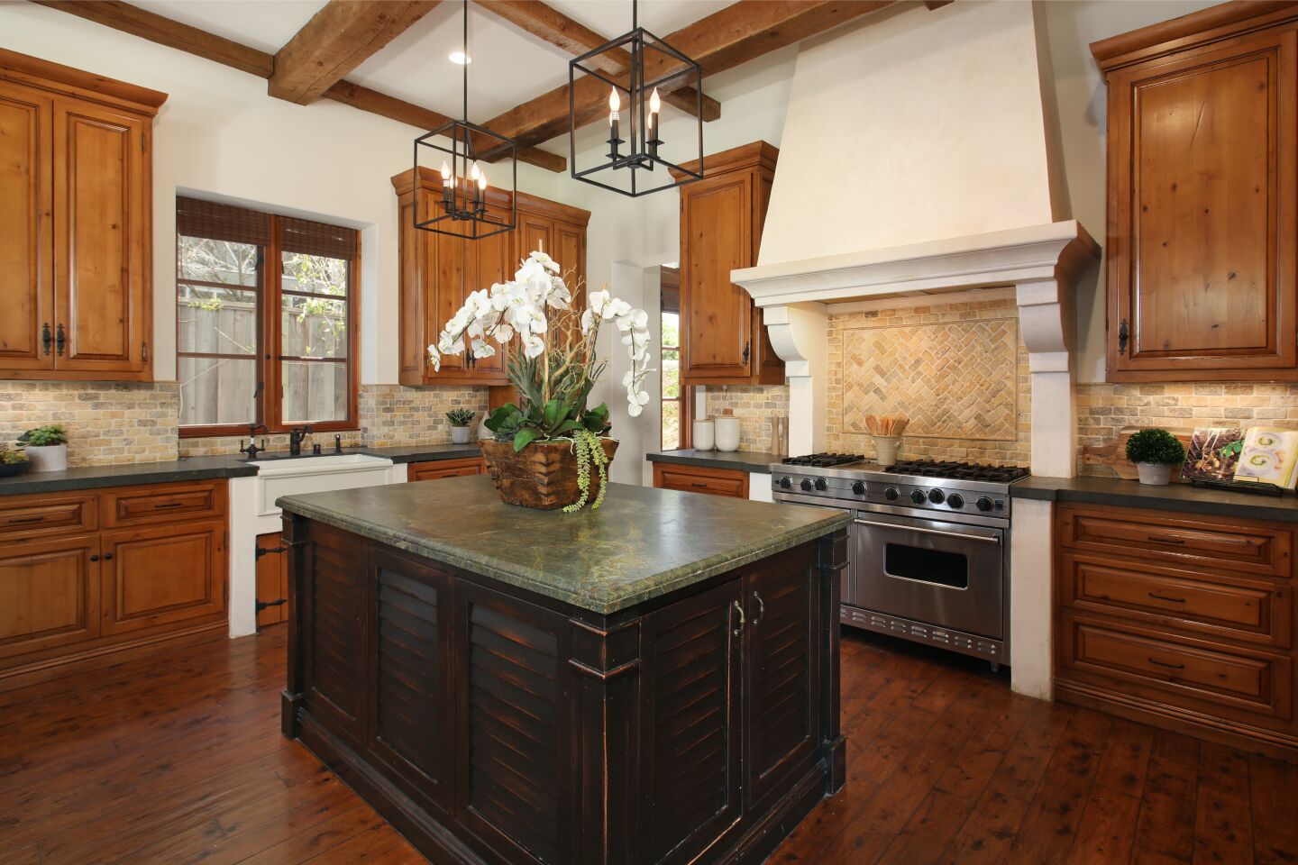 A large island, tile backsplash, wood cabinets and wood floor in the kitchen.