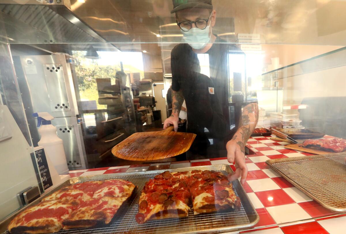 Kyle Lambert stands behind the glass case of his restaurant. In front of him are one pepperoni pizza and one cheese pizza.