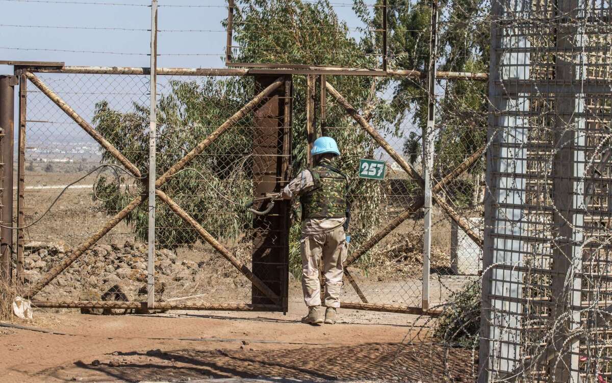 A member of the United Nations Disengagement Observer Force (UNDOF) closes a gate between the Israeli-annexed Golan Heights and the Syrian-controlled territory Thursday. The United Nations confirmed that an armed group captured 43 UN peacekeepers on the Syrian side of the Golan Heights, and said it was doing everything to secure their release.
