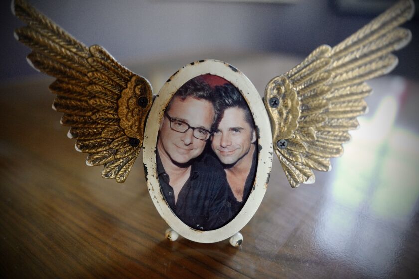 A photograph of Bob Saget and John Stamos together in an angel wing frame.
