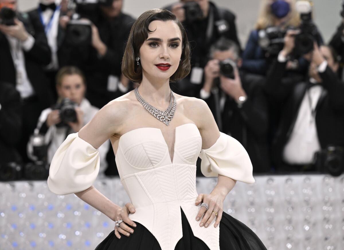 Lily Collins wears an outfit with a white bodice and black skirt