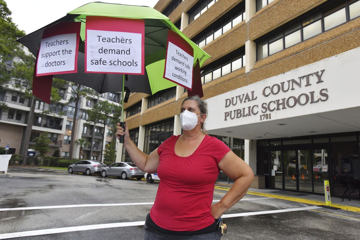 Christine O'Riley, a school teacher and the mother of a child under 12 holds her protest umbrella outside the school board building ahead of their Tuesday evening meeting to discuss the masking issue Aug. 3, 2021. Around 50 people gathered outside the Duval County School Board building in Jacksonville, Fla., in support of having mandatory masking of teachers and students ahead of the school board taking up the issue in their Tuesday evening meeting. Florida's Gov. Ron DeSantis has forbidden mandating masks in Florida's public schools despite CDC recommendations to wear masks due to the recent surge of COVID-19 infections which are particularly high in Northeast Florida. (Bob Self/The Florida Times-Union via AP)