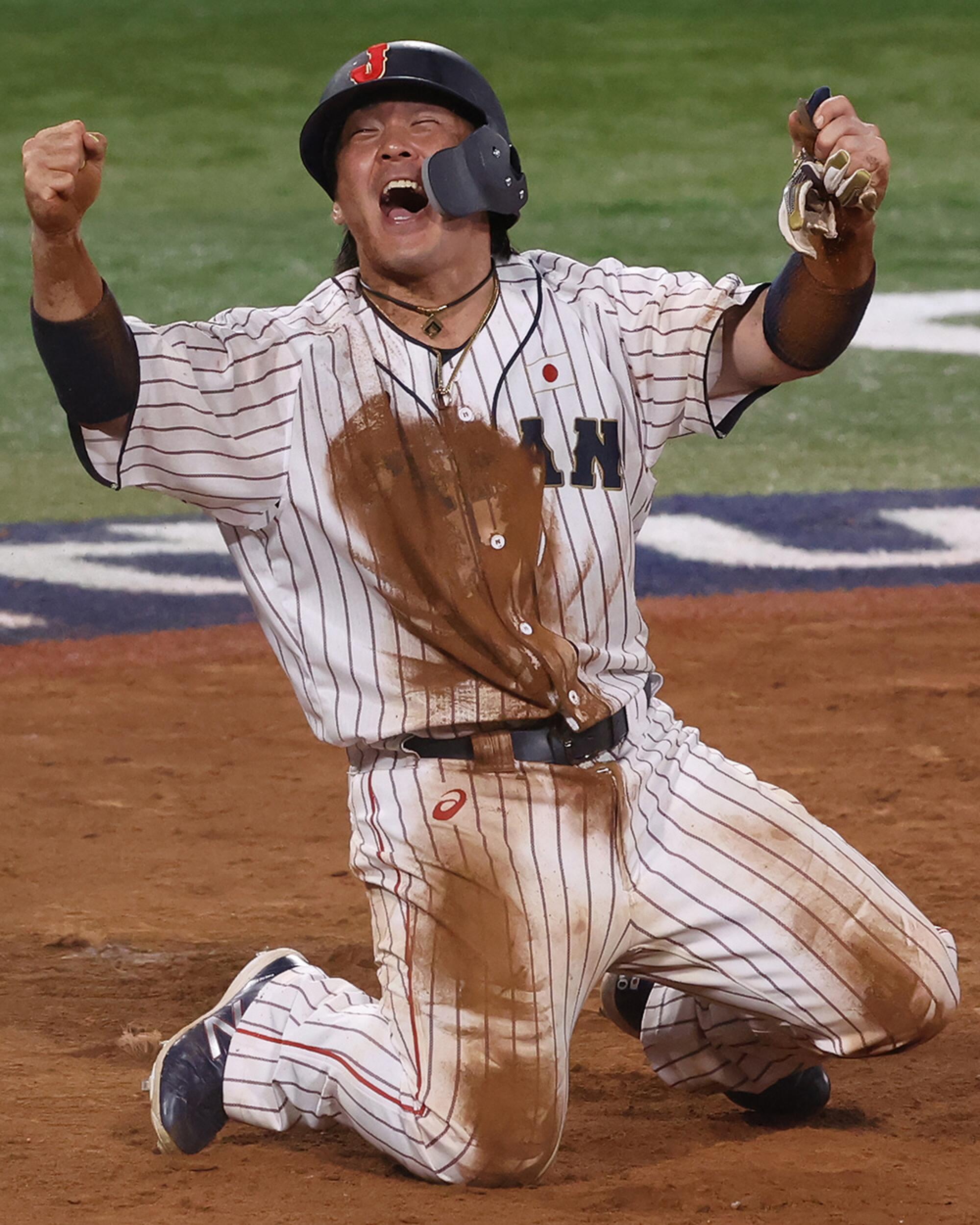Takuya Kai, kneels, covered with dirt, shouting with his arms above his head.