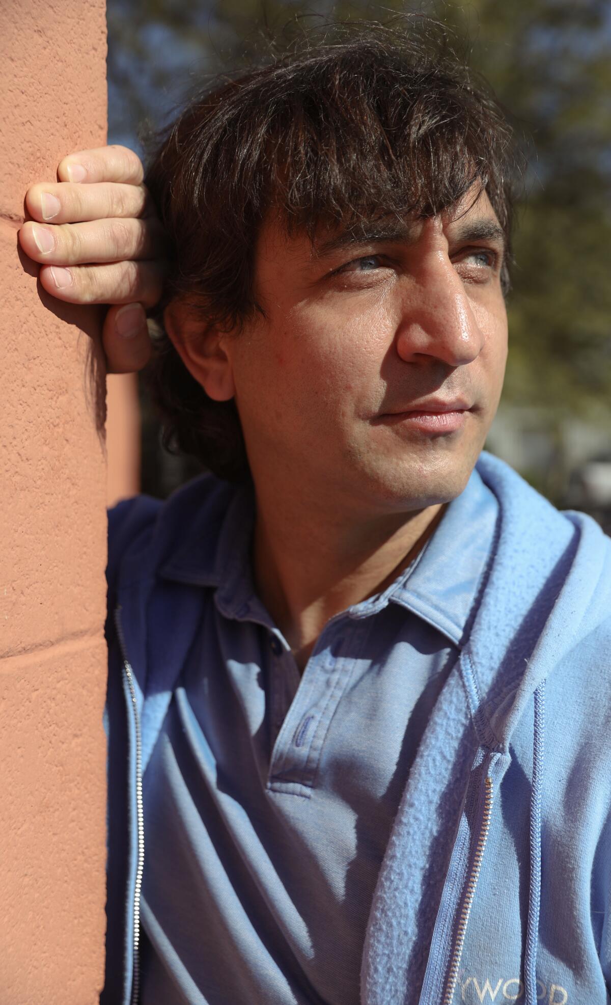 A man posing against a red brick wall. 