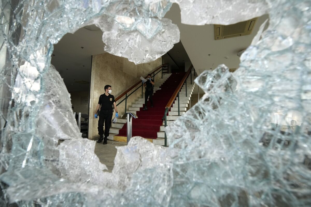 Forensic investigators, framed by a broken window, survey the damage in Brasilia's Supreme Court building.