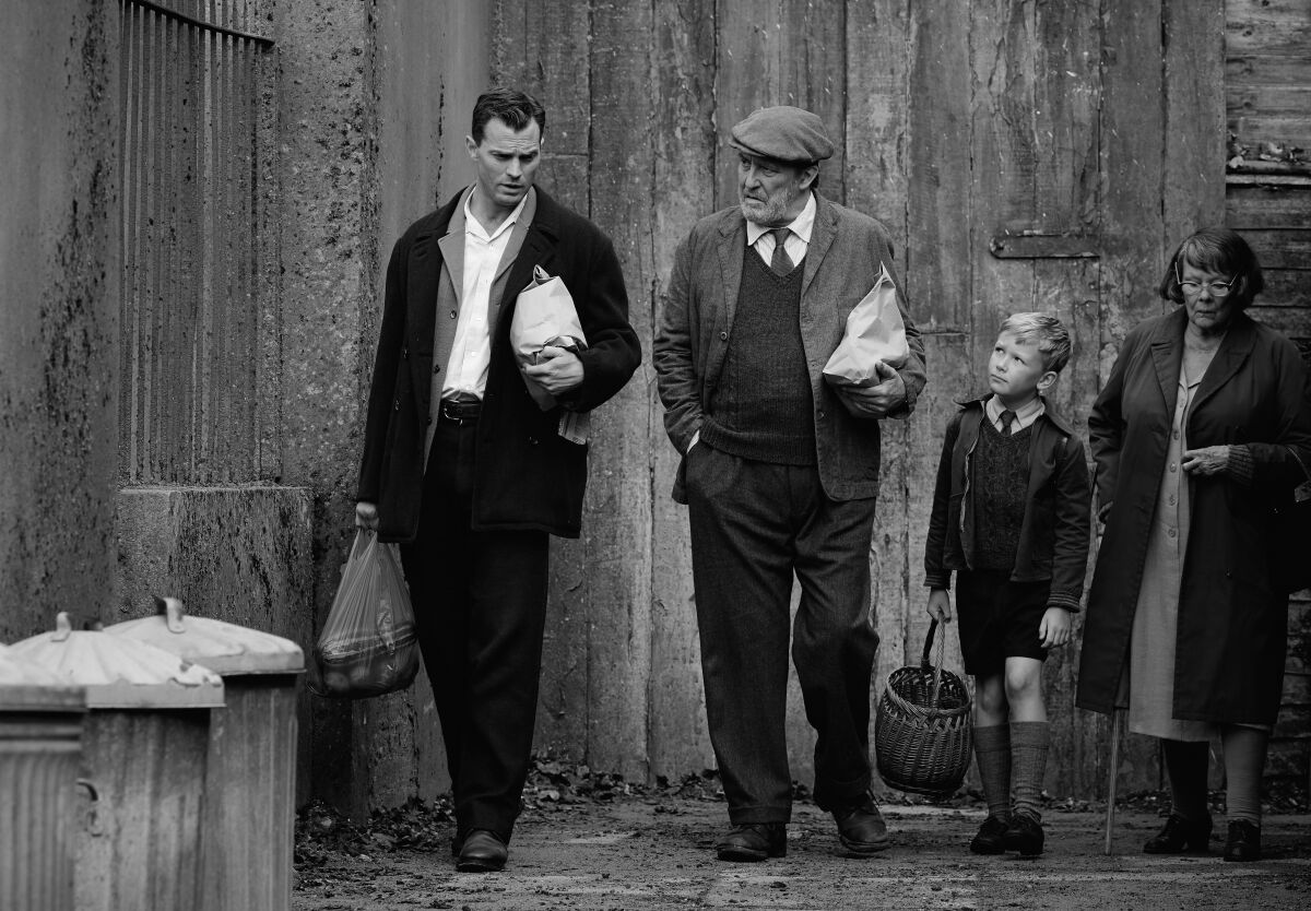 A black-and-white still from "Belfast" shows three adults and a boy walking past trash cans.