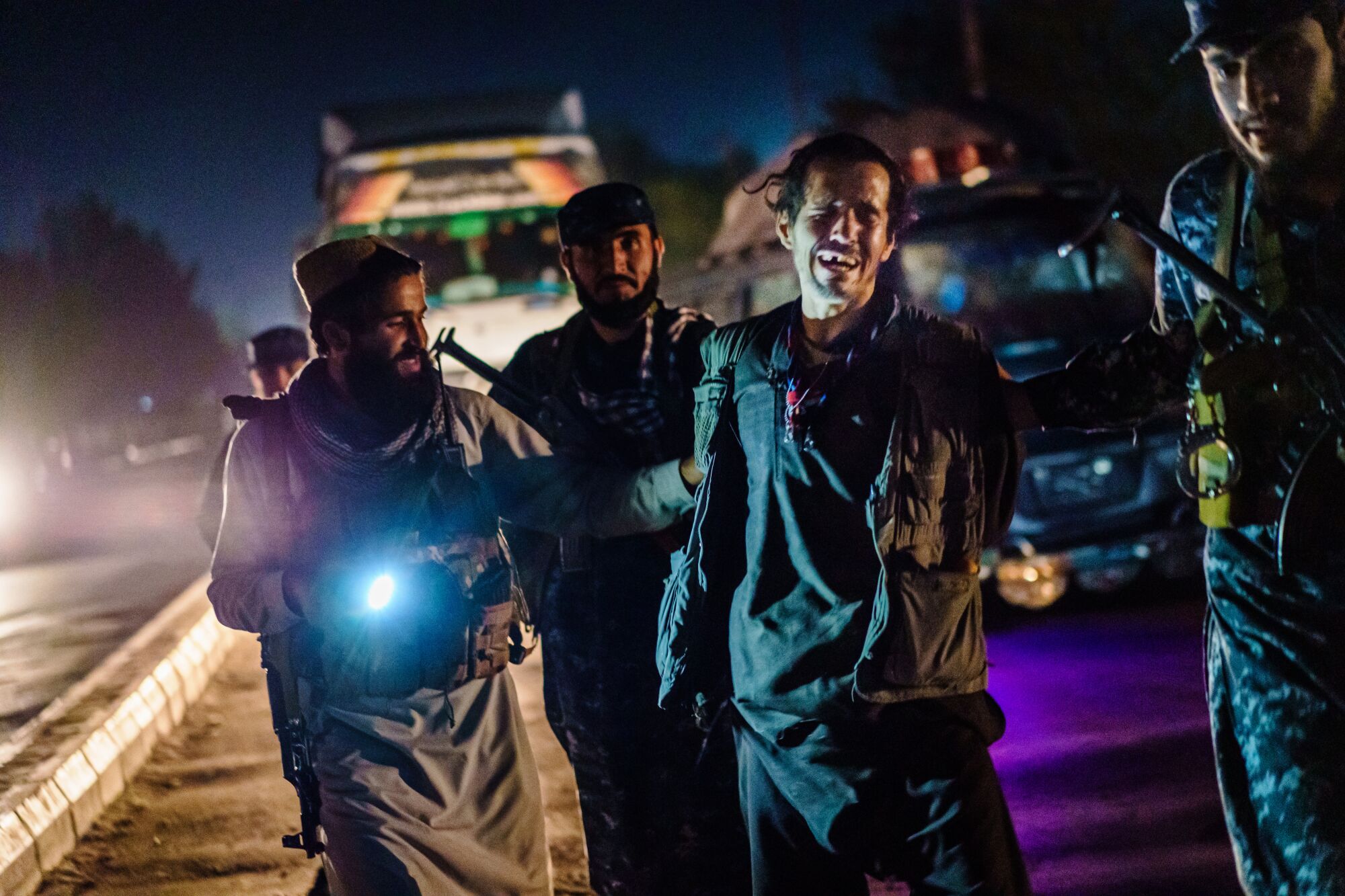 On a street at night, men with weapons pull along a crying man.