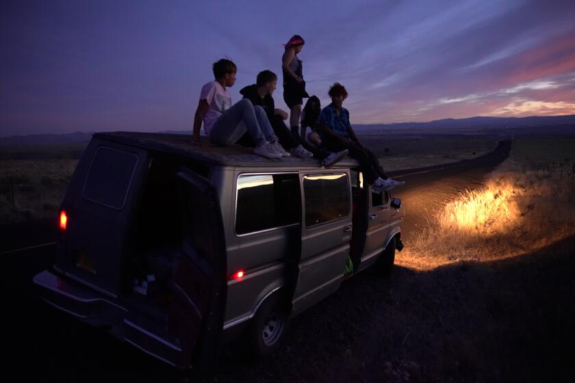 Several friends sit on the top of a van at night.