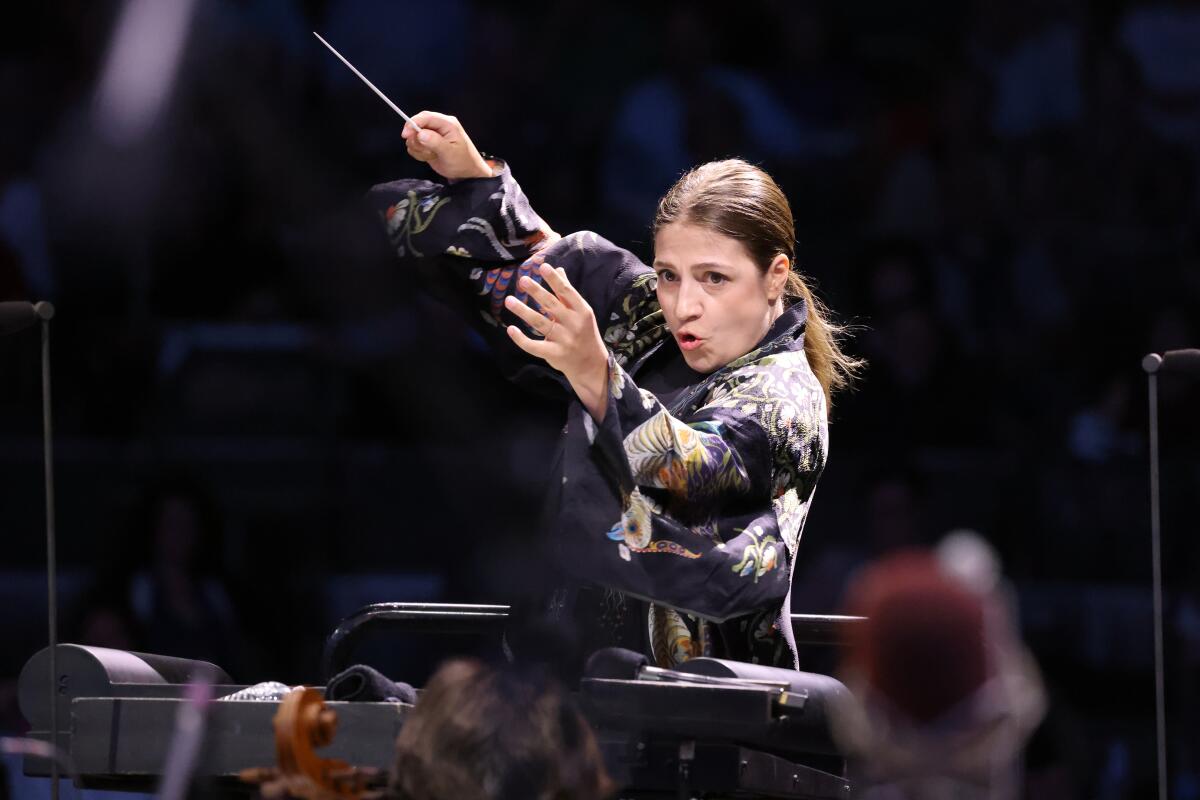 A female conductor raises her arms and her baton.