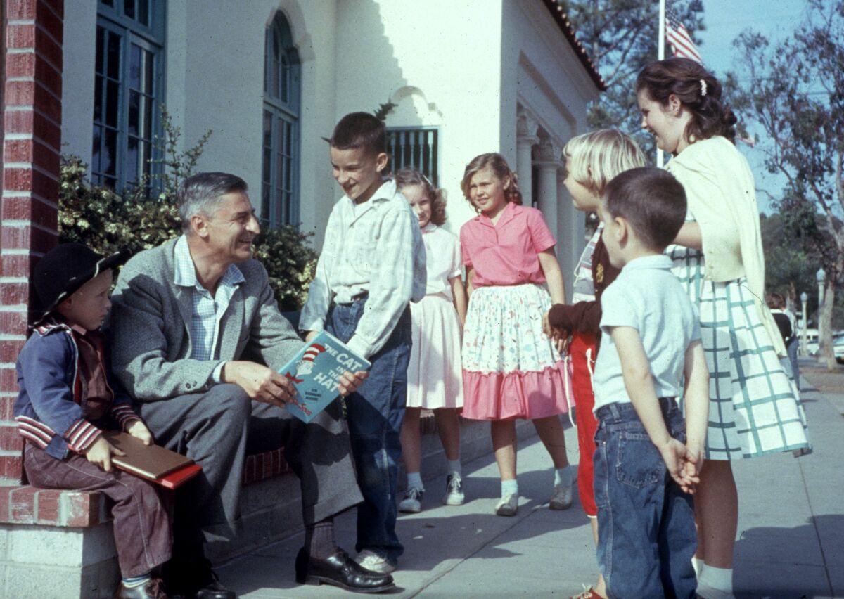 Author Dr. Seuss holds a copy of "The Cat in the Hat" and is surrounded by kids.