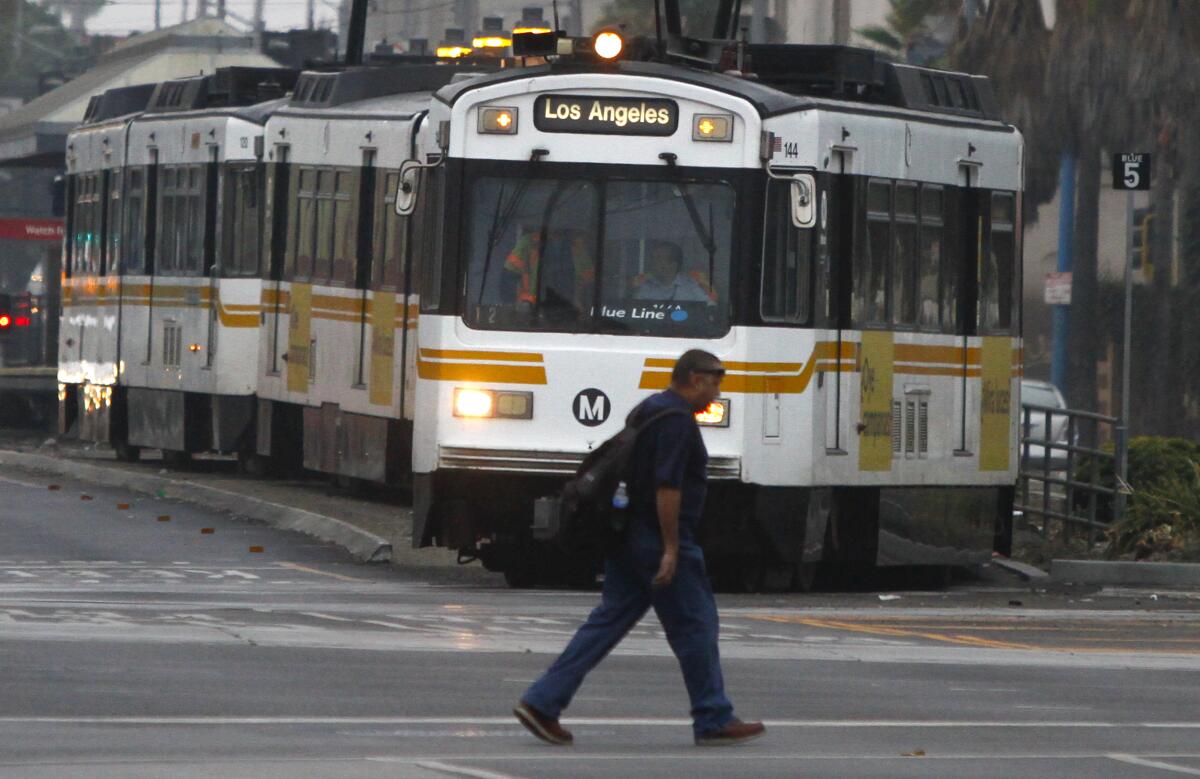 A pedestrian safely crosses the road while a METRO Blue line train makes a turn in downtown Los Angeles.