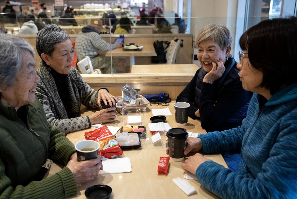 Horizontal image of four women seated at a rectangular table in a restaurant, talking.