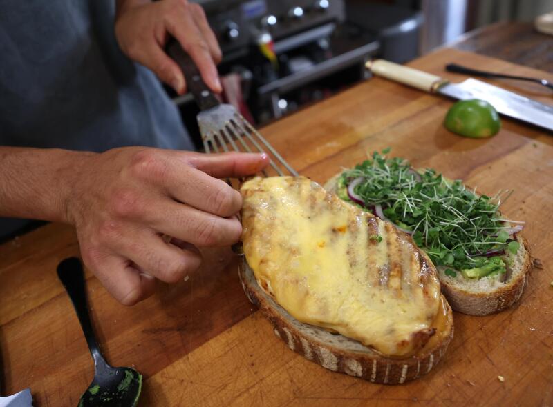 A closeup of an open chicken sandwich with greens and melted cheese