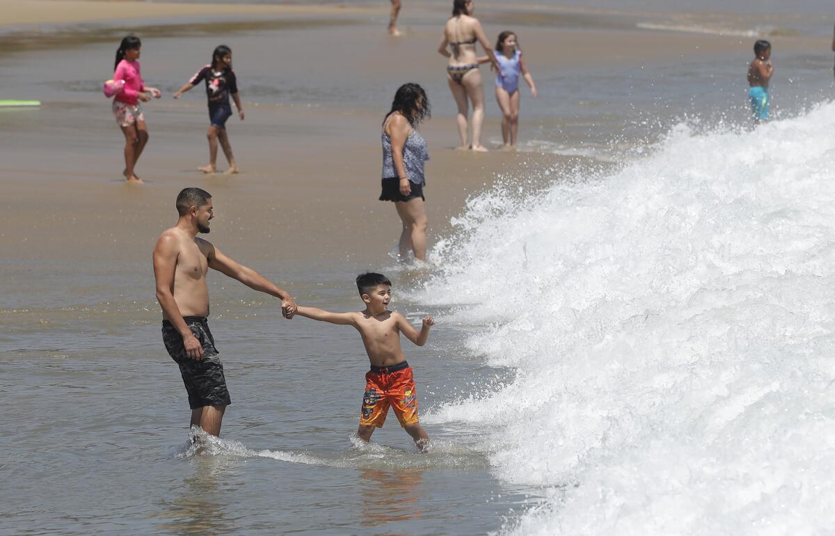 Ricardo Morales, left, and his son, Marcos, play in the frothy shore break at Corona del Mar State Beach on Tuesday.