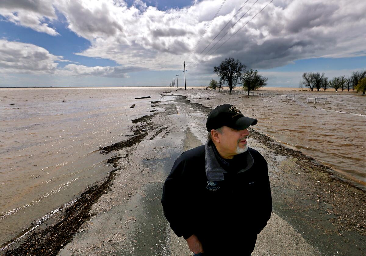 A man stands on a flooded farm road.