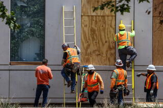 People in orange vests climb ladders next to boarded-up windows.