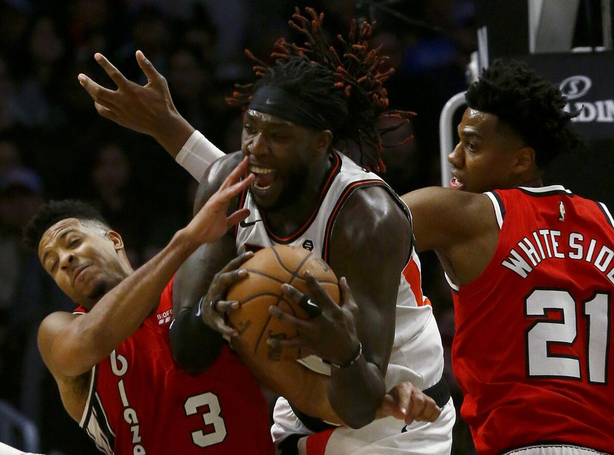 Clippers forward Montrezl Harrell pulls down a rebound between Portland Trail Blazers' CJ McCollum, left, and Hassan Whiteside in the fourth quarter at Staples Center on Tuesday.