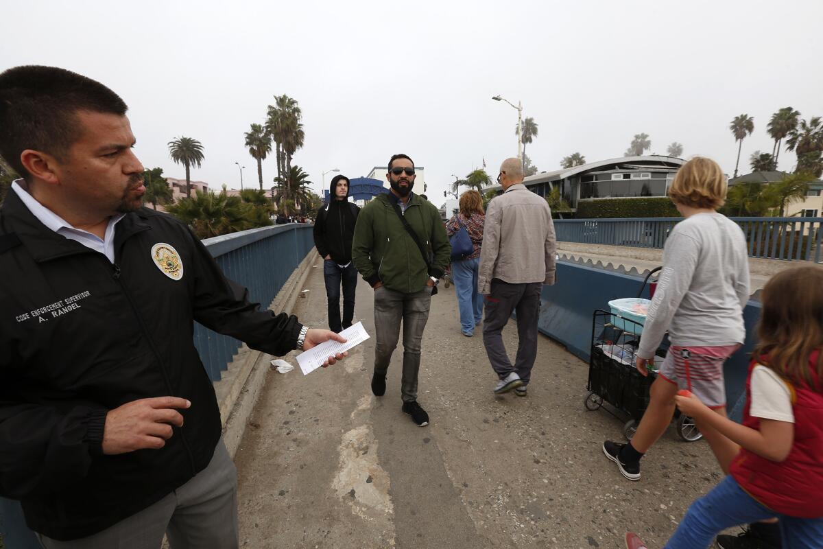 Armando Rangel, left, a code enforcement supervisor for the city of Santa Monica, points to the cart of a street vendor on the Santa Monica Pier this month.