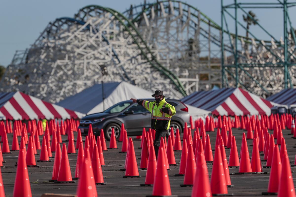 A person in a reflective jacket gestures in a parking lot filled with orange cones.