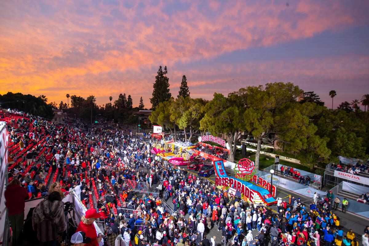 A dawn sky over the starting point of the Rose Parade with people looking at colorful floats