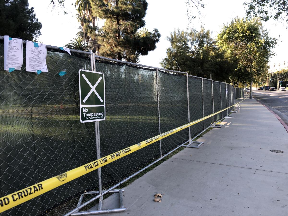 Yellow police tape reading "Do Not Cross" stands before a green construction fence circling Echo Park Lake