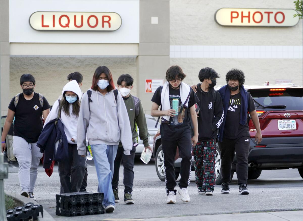 Teenagers wearing masks walk through a parking lot in downtown Los Angeles
