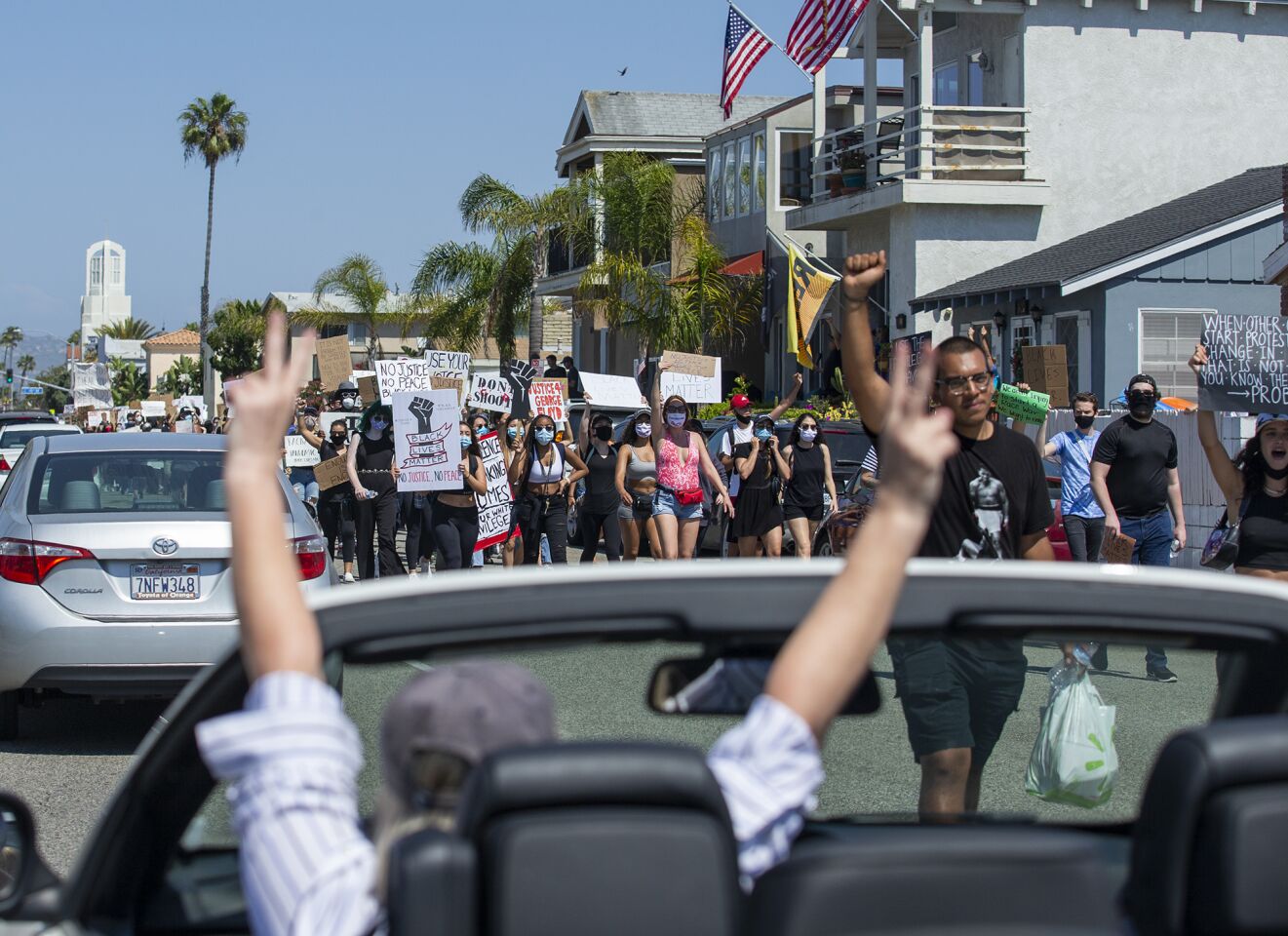 Demonstrators walk down Balboa Boulevard as a passing motorist flashes peace signs on Wednesday.