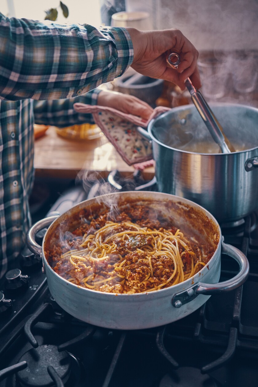 A cook makes a giant pot of pasta with marinara sauce.