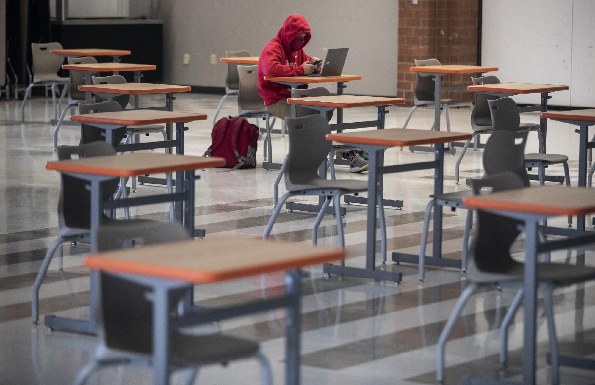 A lone student sitting at a desk in a group of spaced-out desks