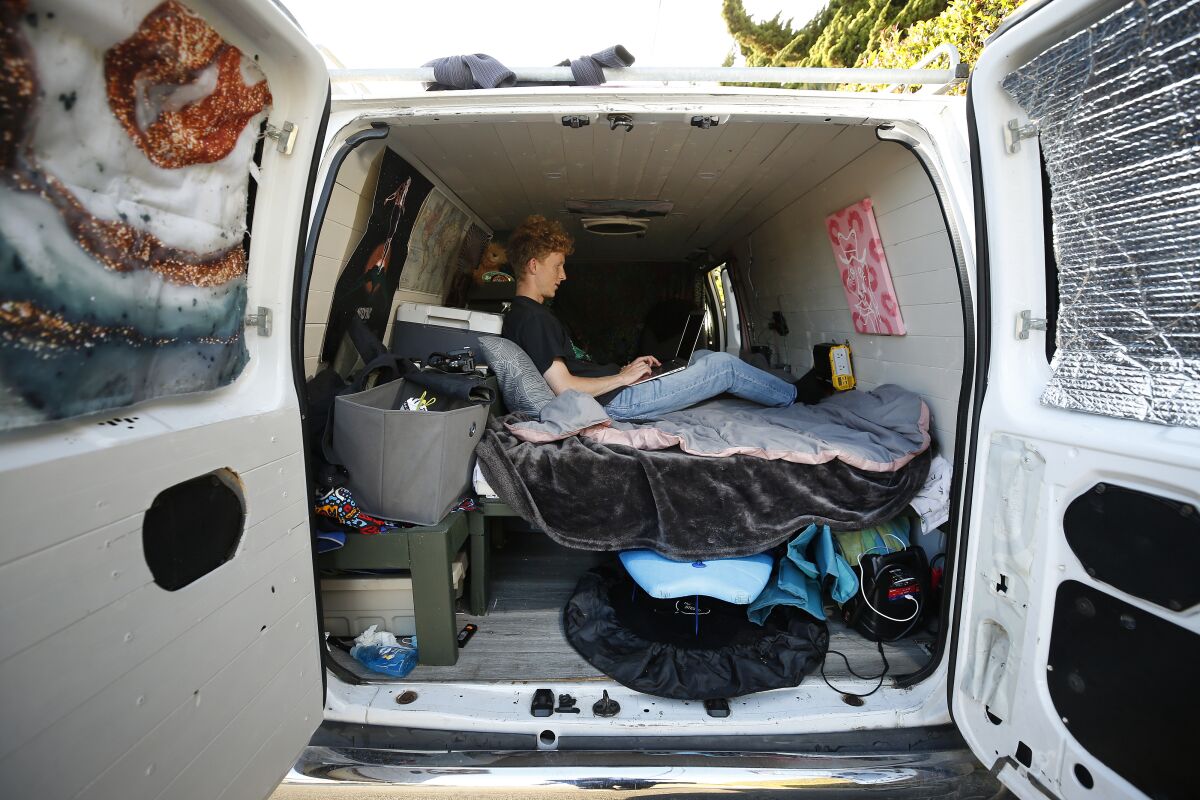 a young man sits on a bed inside the back of a large white van