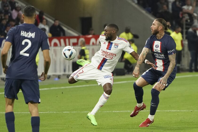 Lyon's Karl Toko Ekambi, left, and PSG's Sergio Ramos challenge for the ball during the French League One soccer match between Lyon and Paris Saint Germain at Groupama stadium in Decines, outside Lyon, central France, Sunday, Sept. 18, 2022. (AP Photo/Laurent Cipriani)