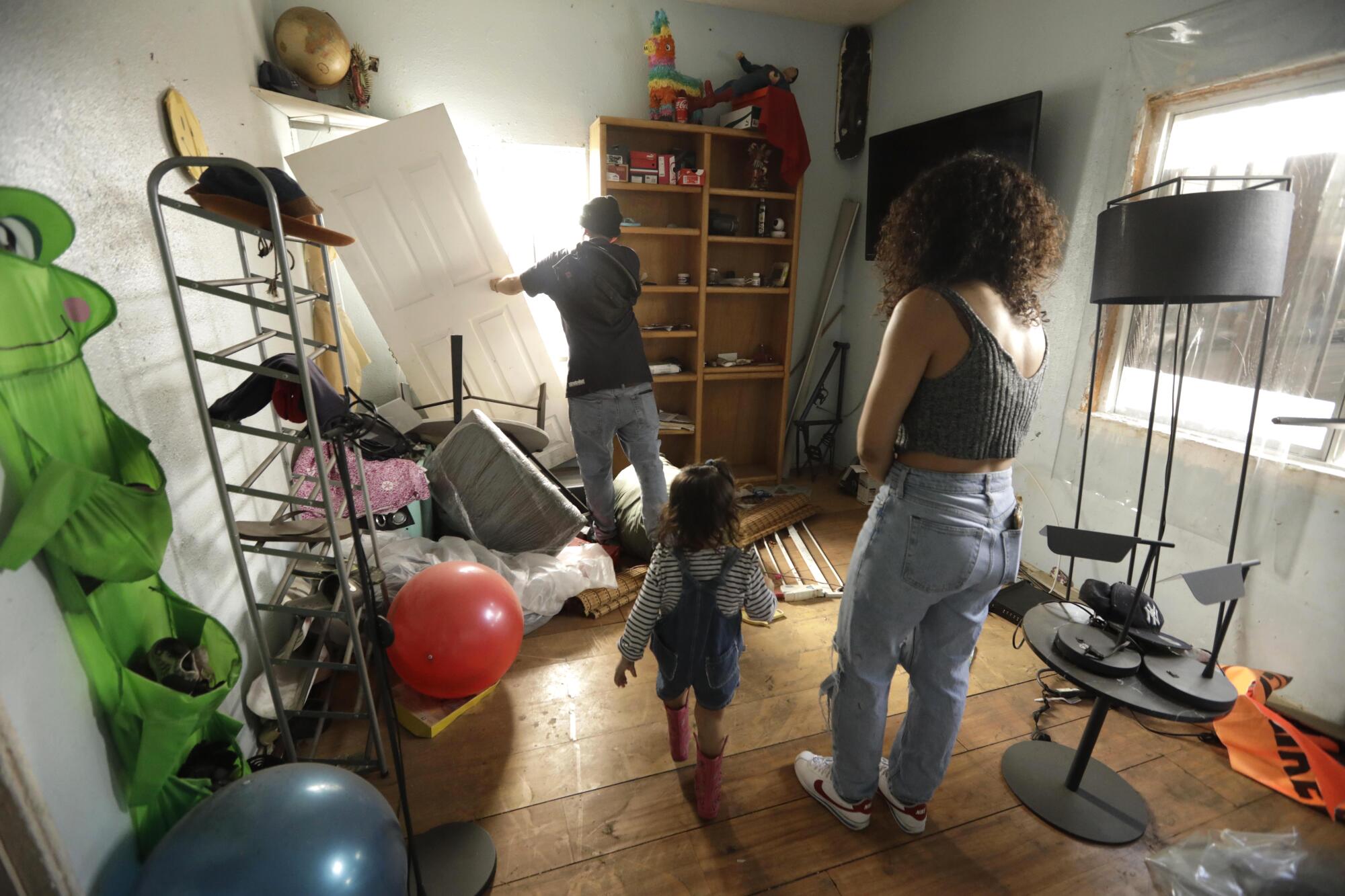 Two adults and a child in a home with belongings strewn about