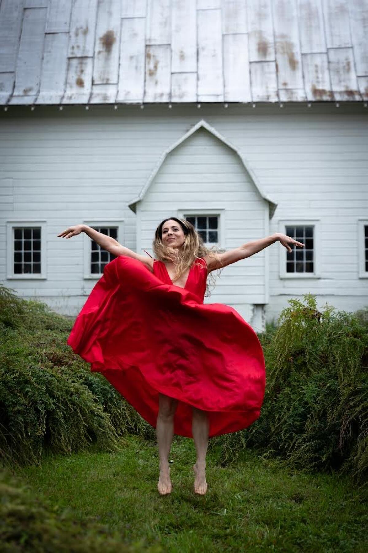 Moon Unit Zappa, in a red dress, jumps with arms outstretched.