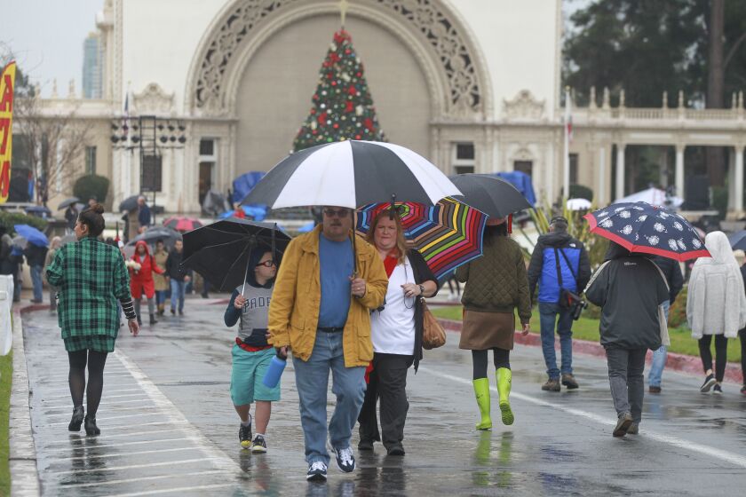 With the Spreckels Organ Pavilion in the background, people walk in the rain during the second day of December Nights at Balboa Park on Saturday, December 7, 2019 in San Diego, California.