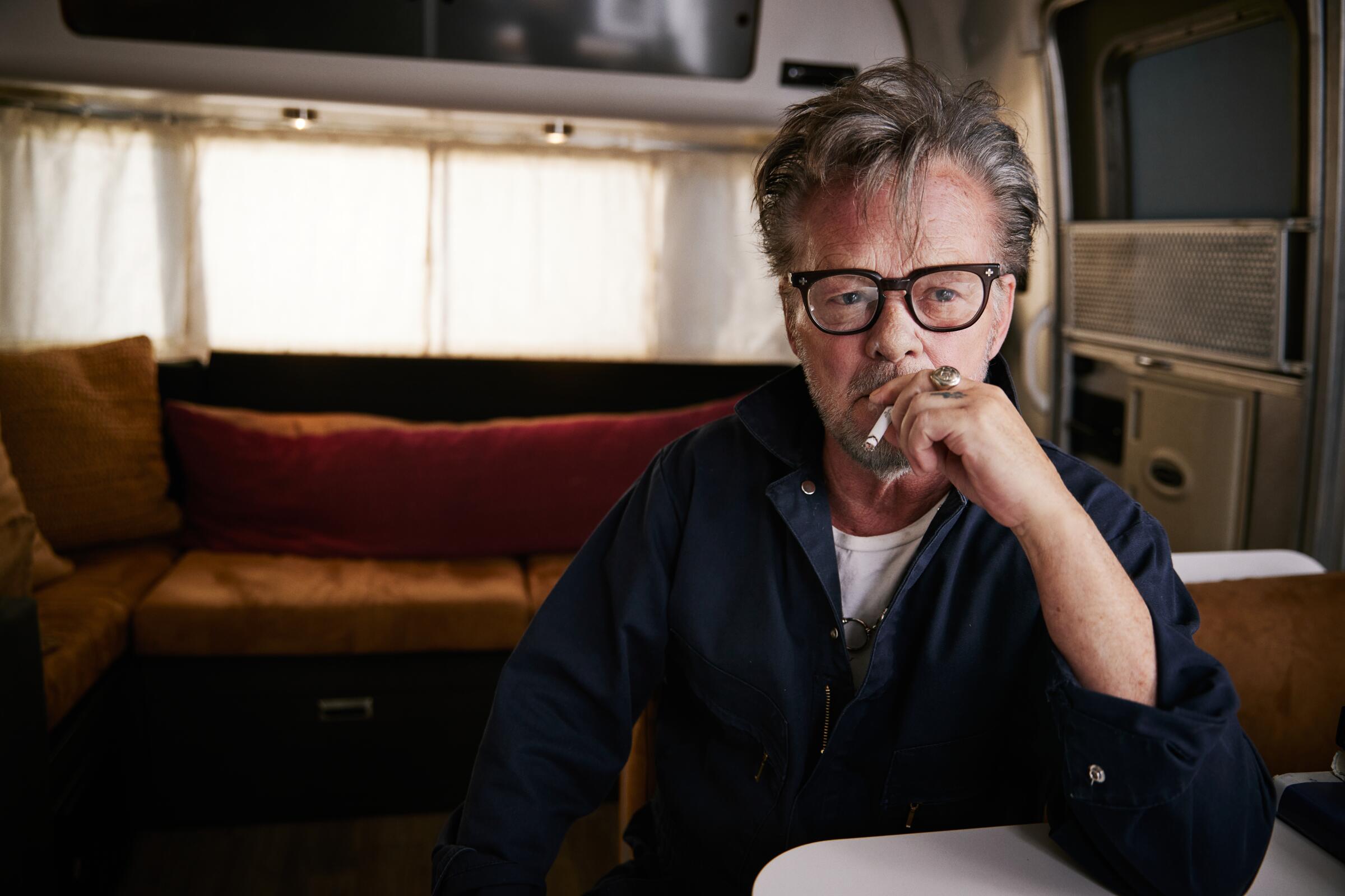 A man wearing glasses, smoking in a trailer.