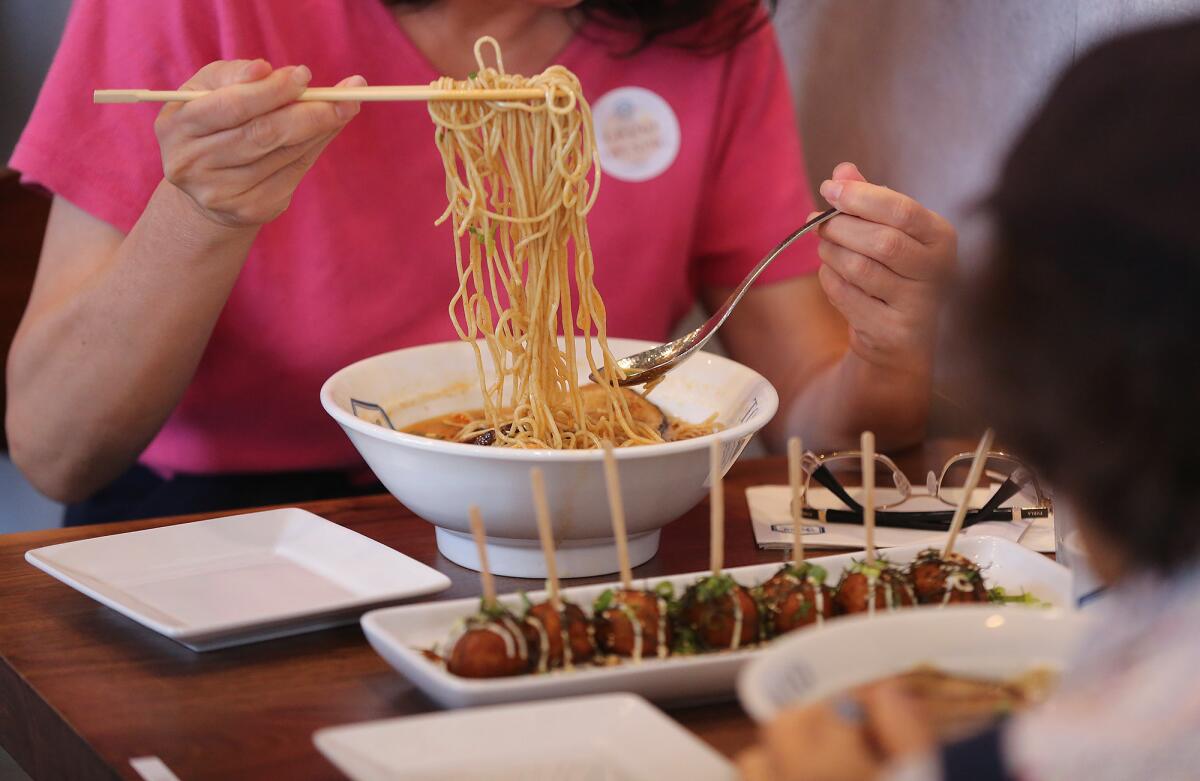 A guest cools off a portion of fresh ramen during opening of Rakkan Ramen at the District at Tustin Legacy.