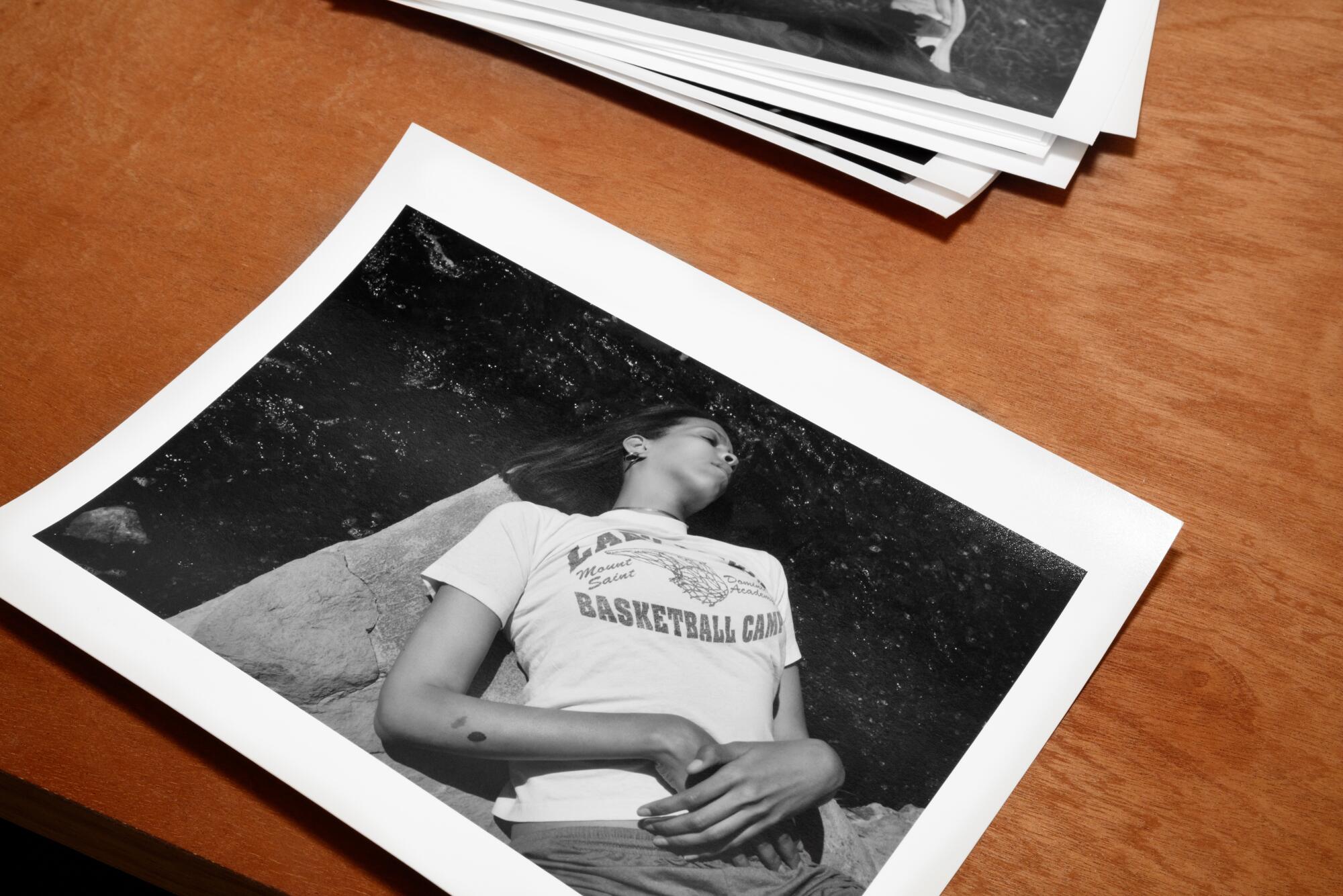Image of a black and white photograph of Lacey in a basketball camp t-shirt lying on a rock surrounded by water.