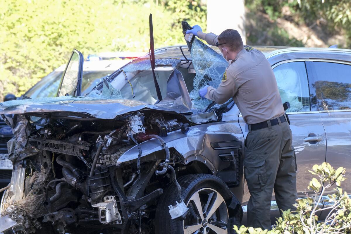 A law enforcement officer looks over a damaged vehicle following a rollover crash involving golfer Tiger Woods. 