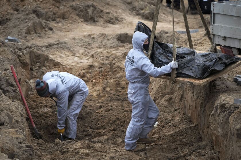 Men wearing protective gear exhume the bodies of civilians killed during the Russian occupation in Bucha, on the outskirts of Kyiv, Ukraine, Wednesday, April 13, 2022. (AP Photo/Efrem Lukatsky)