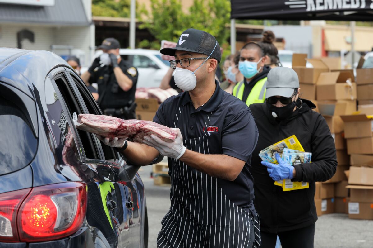 Mark Mendoza places a large package of meat in the rear side window of one of the hundreds of vehicles that showed up to a food distribution in Escondido on April 11.